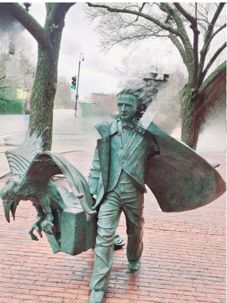 Fanciful statue of Edgar Allan Poe, billowing coat in the wind, walking with a strong stride, scary raven opening his briefcase. He's on a modern city scape, walking on brick with trees and a stoplight behind him and hair blowing in the wind. Copper is green with age.