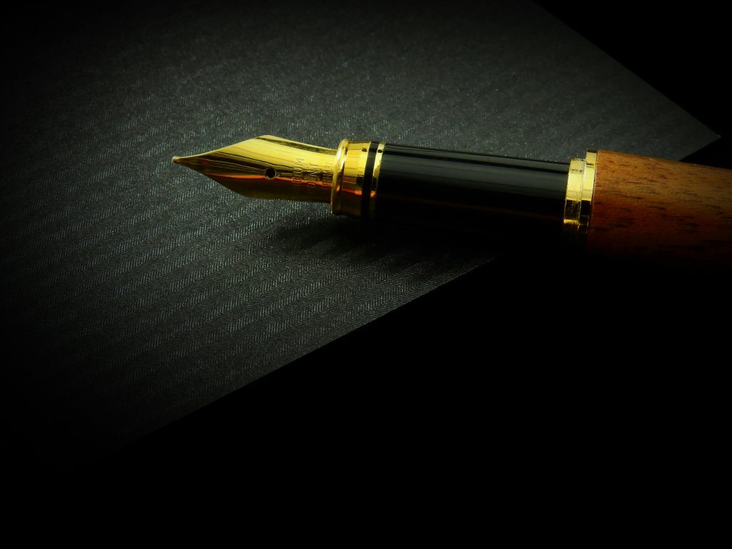 Fountain pen made of metal and wood, on a black canvas with light shining on it.