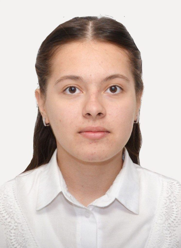 Young Central Asian woman with straight brown hair, brown eyes, small silver earrings, and a white collared shirt.