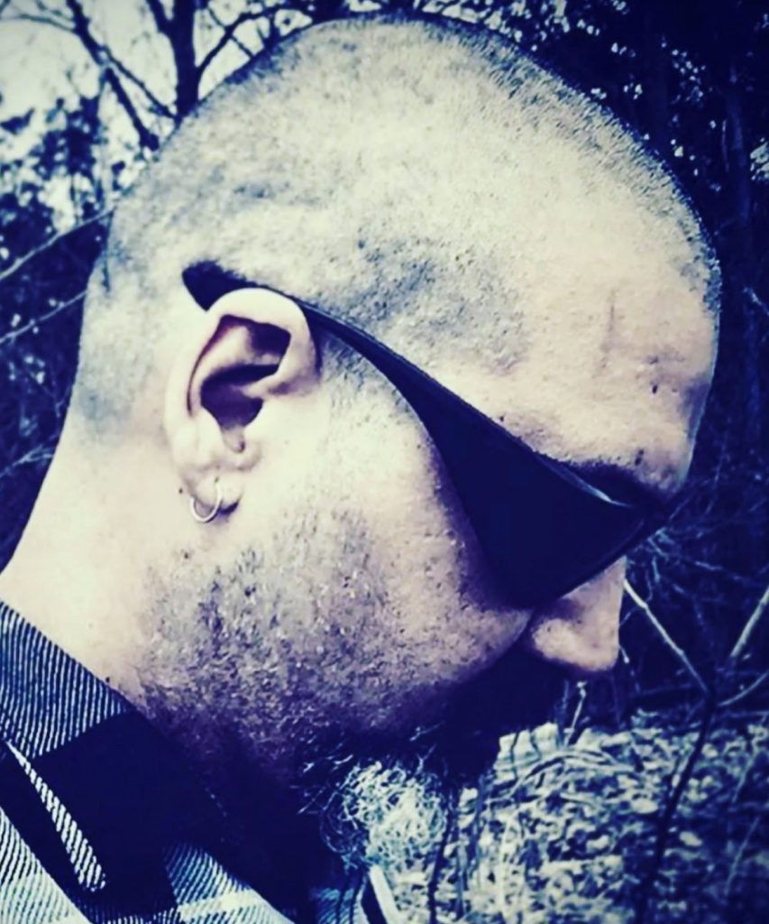 Profile photo of the poet from the left. He's a middle aged white guy with an earring, sunglasses, and small beard. 