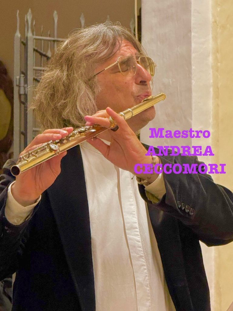 Photo of Maestro Andrea Ceccomori playing a brass flute with his eyes closed. He's in a suit with a buttoned coat and white shirt. 