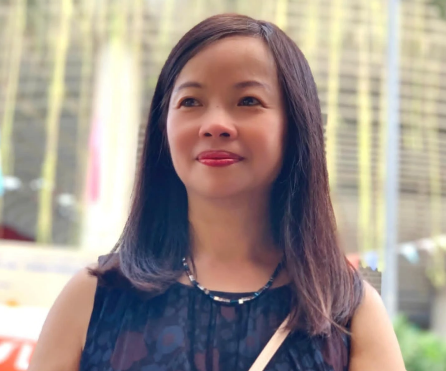 East Asian young woman with long dark hair, a necklace, and a dark patterned sleeveless blouse.