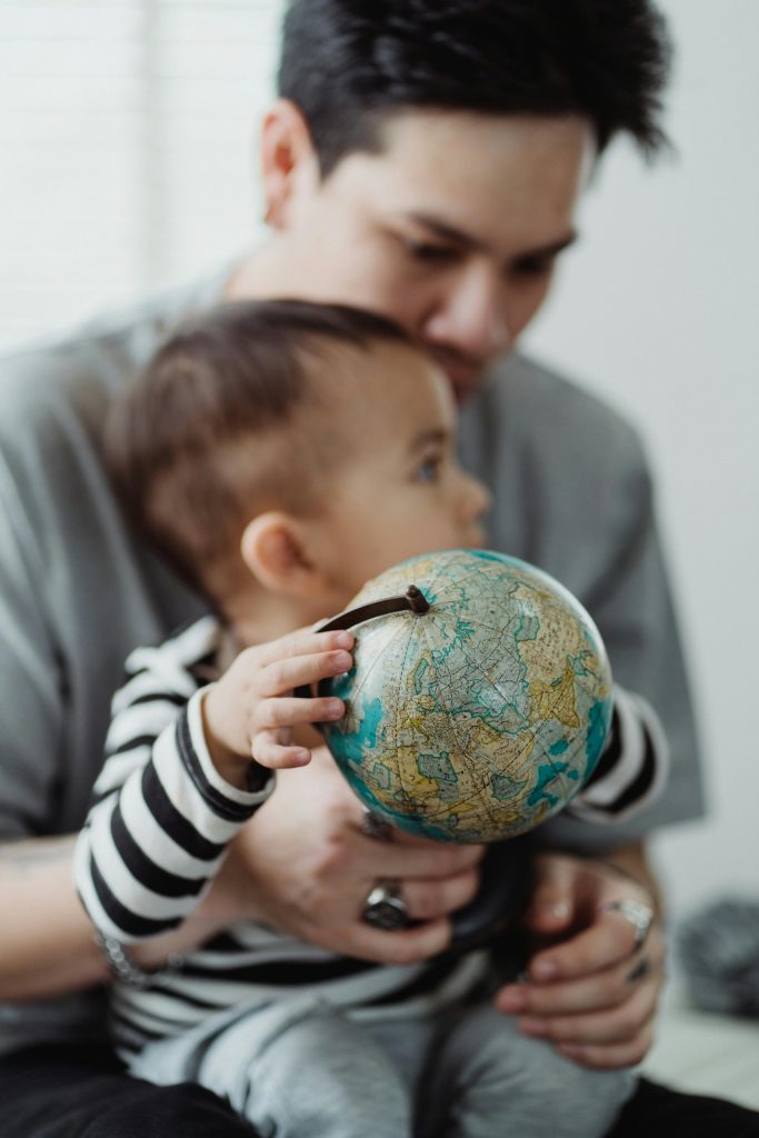 East Asian man with dark hair holds a baby who's holding a globe.