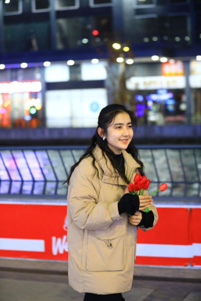 Young Central Asian woman with long curly dark hair, a thick brown coat, and a handful of red tulips