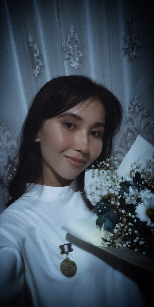 Central Asian woman with long dark hair, white collared blouse, holding a bouquet of white daisies and baby's breath.