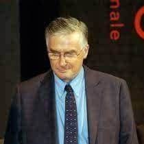 Older white man with reading glasses and a suit and tie.