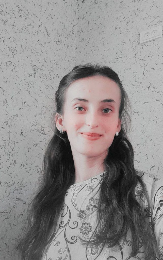 Central Asian teen girl with long dark hair, earrings, and a gray and black floral blouse.