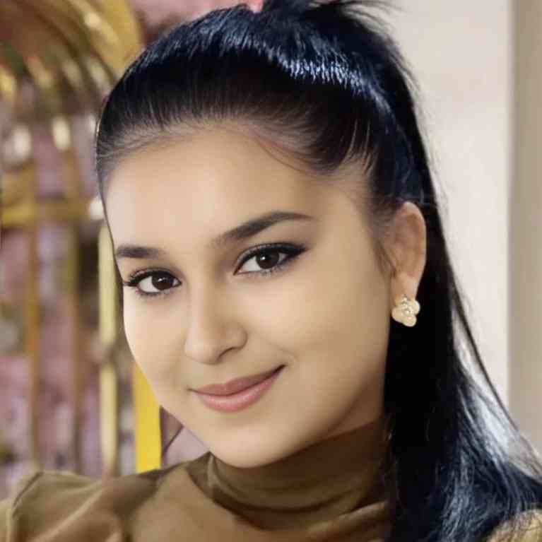 Young Central Asian woman with long dark hair and earrings and a brown turtleneck.