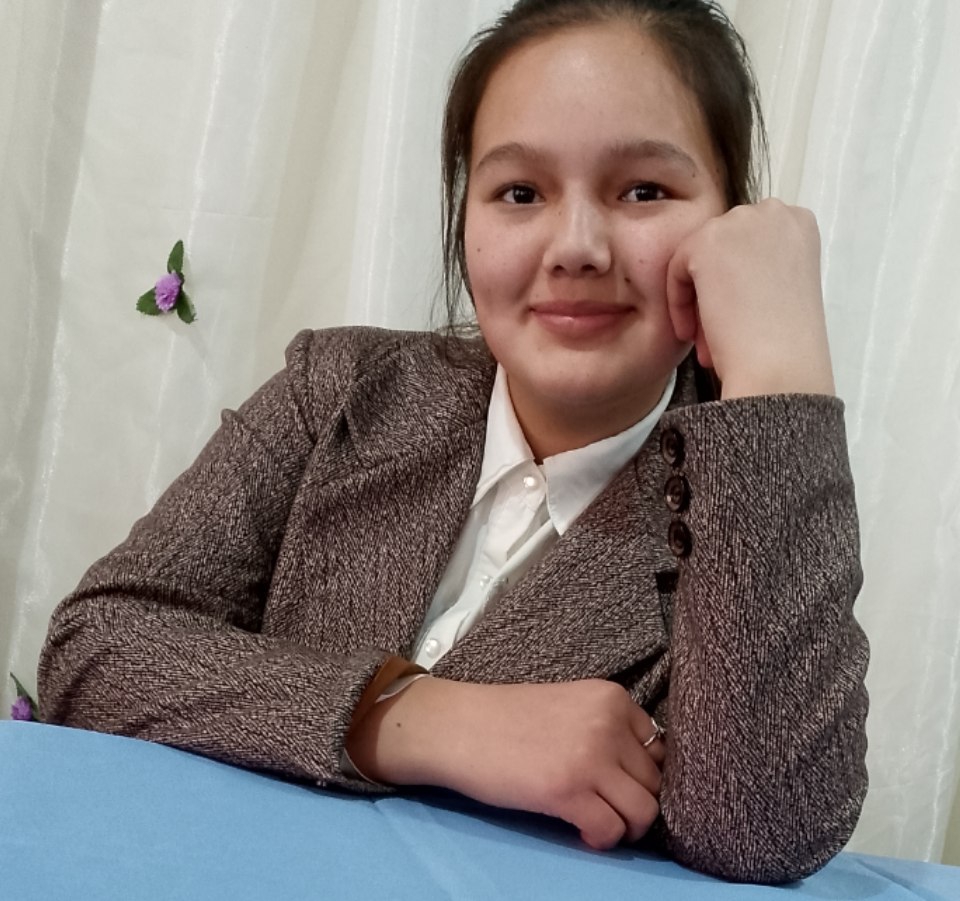 Central Asian young woman with straight dark hair and a tan coat and white collared shirt.