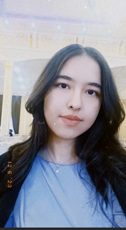 Young Central Asian woman with straight dark hair and brown eyes. She's in a blue top and black coat and tiny necklace.