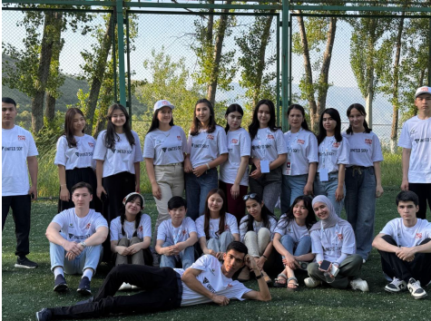 Various young adult students in white tee shirts and jeans out on a lawn with trees in the background.