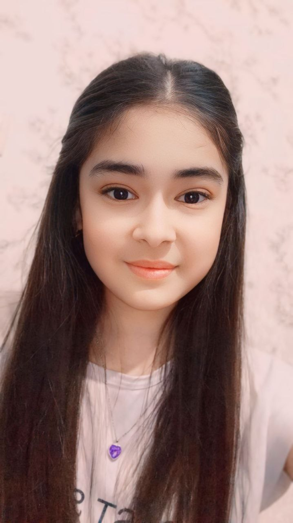 Young Central Asian woman with long dark hair, brown eyes, a small necklace, and a white tee shirt.