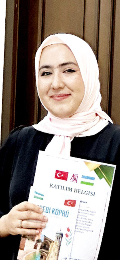 Central Asian woman with a pink headscarf and black dress holding a certificate.