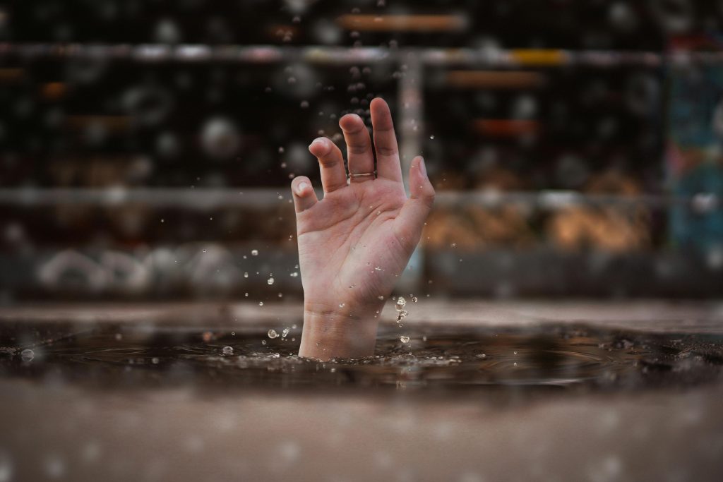 Light skinned hand reaching out of water, maybe grabbing for rescue? Ring on the middle finger.