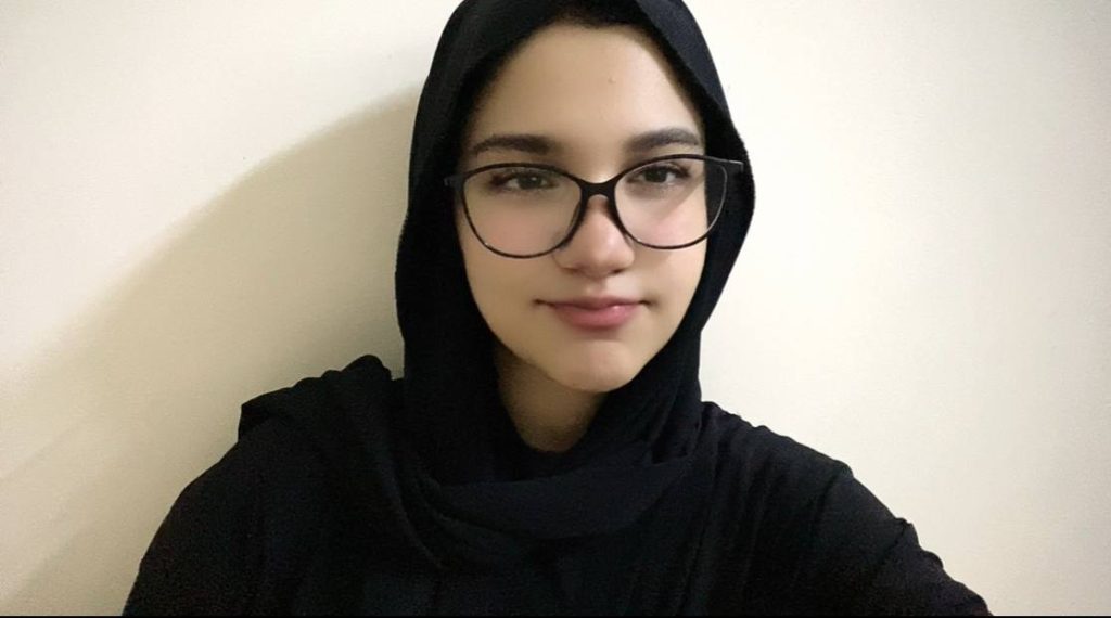 Central Asian teen girl in a black headscarf and sweater and black reading glasses.