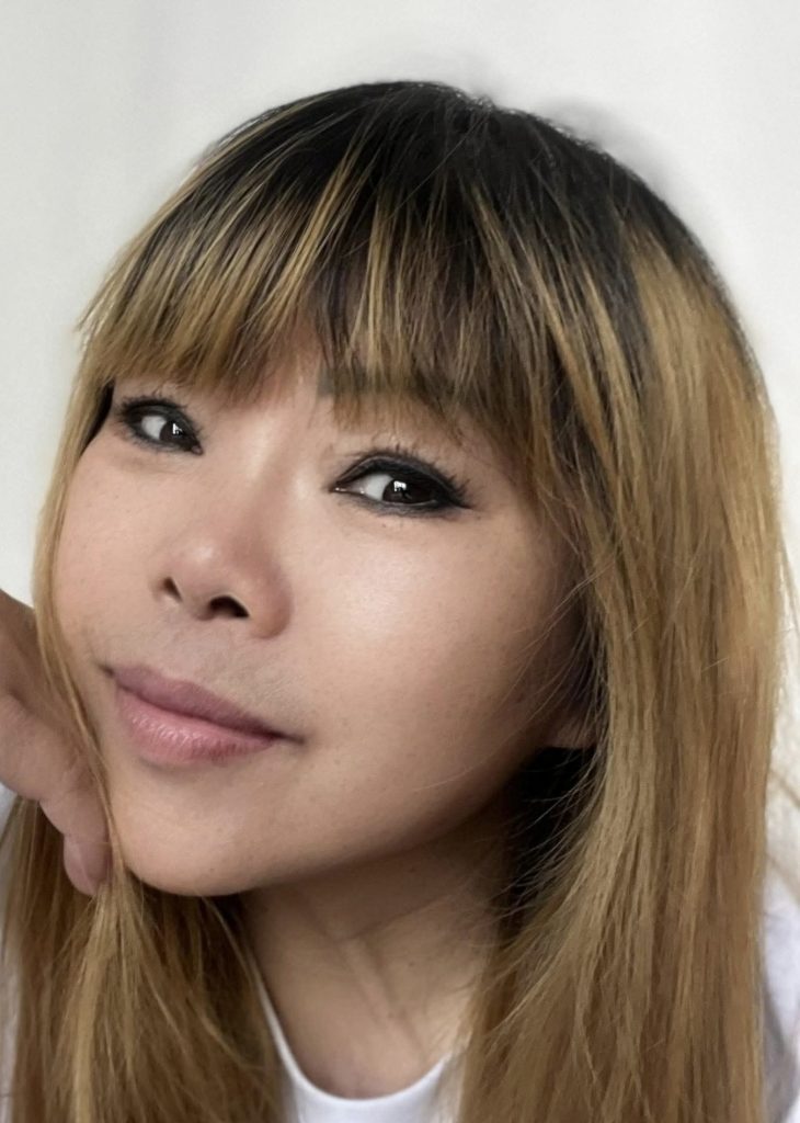 Young East Asian woman's face closeup. She's got dark brown hair, brown eyes, and a small smile.