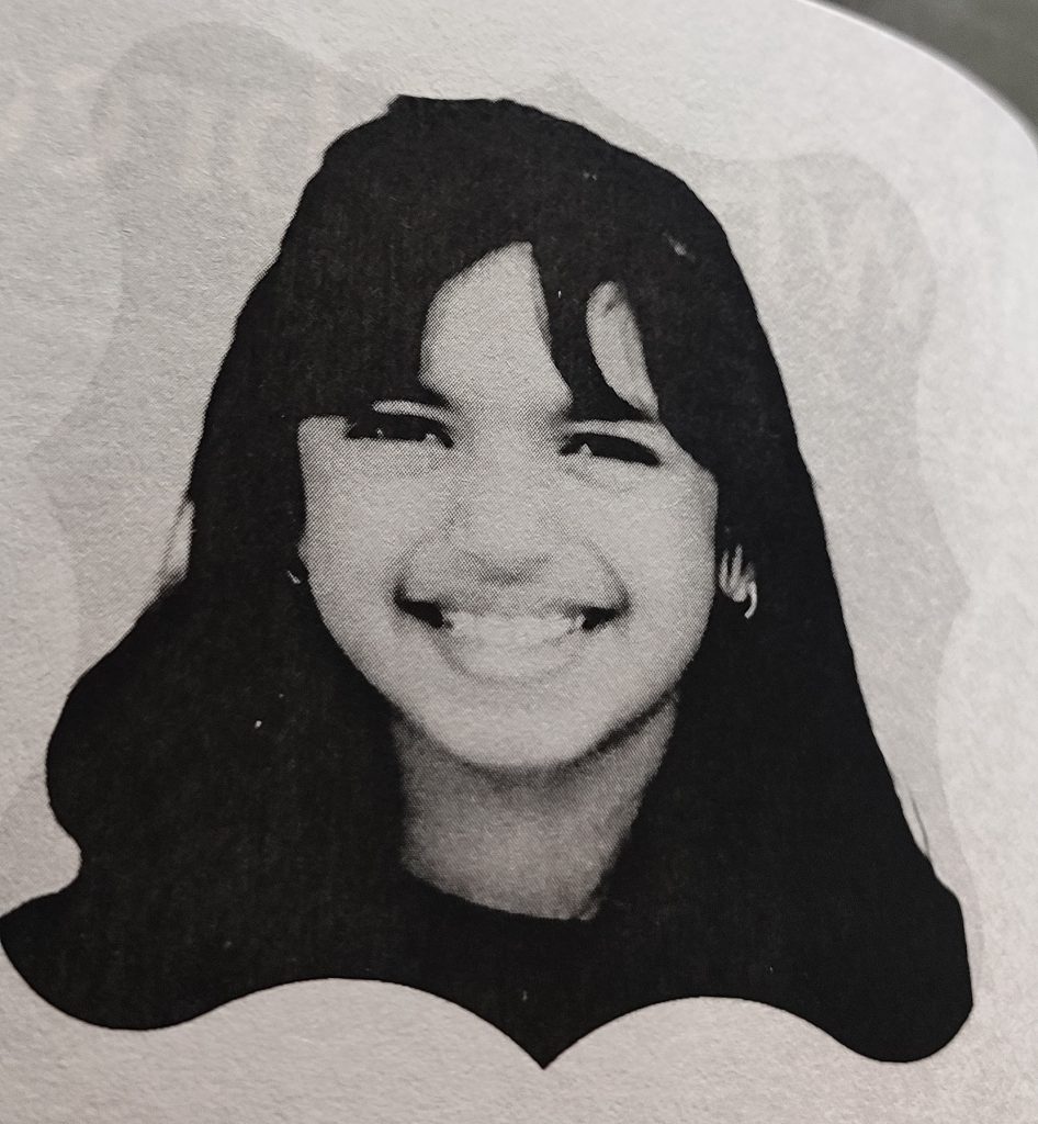 Black and white photo of a young smiling woman with thick dark hair and small earrings.
