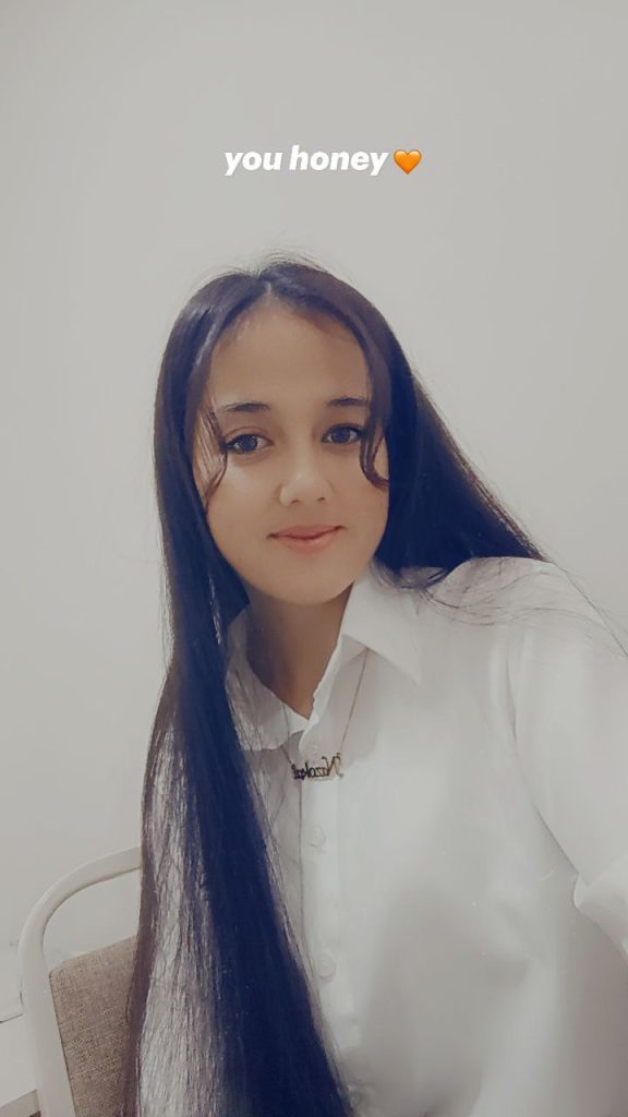 Central Asian young woman with a white collared shirt, a necklace, and long dark hair. 
