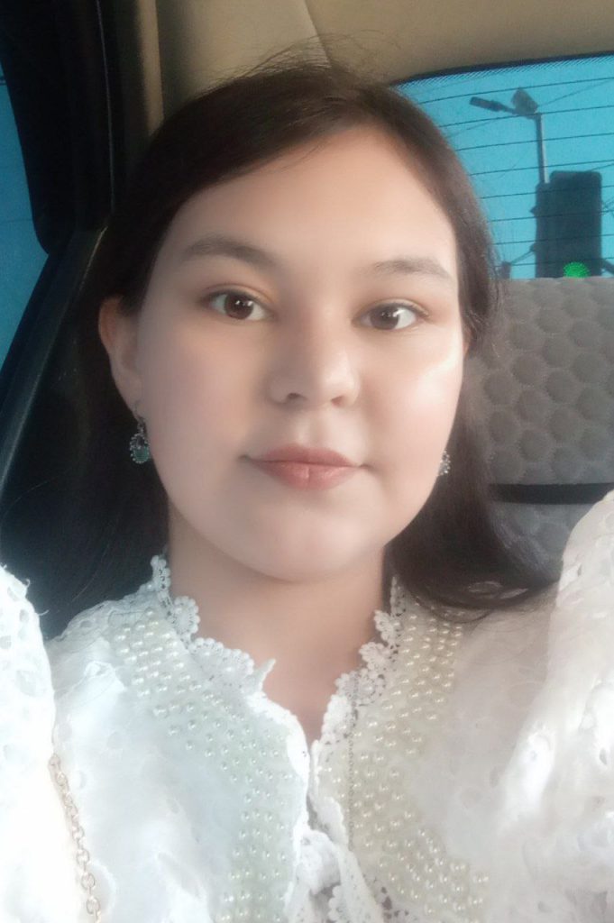 Young Central Asian woman with a ruffled white blouse and earrings and long dark hair in the back seat of a car. 