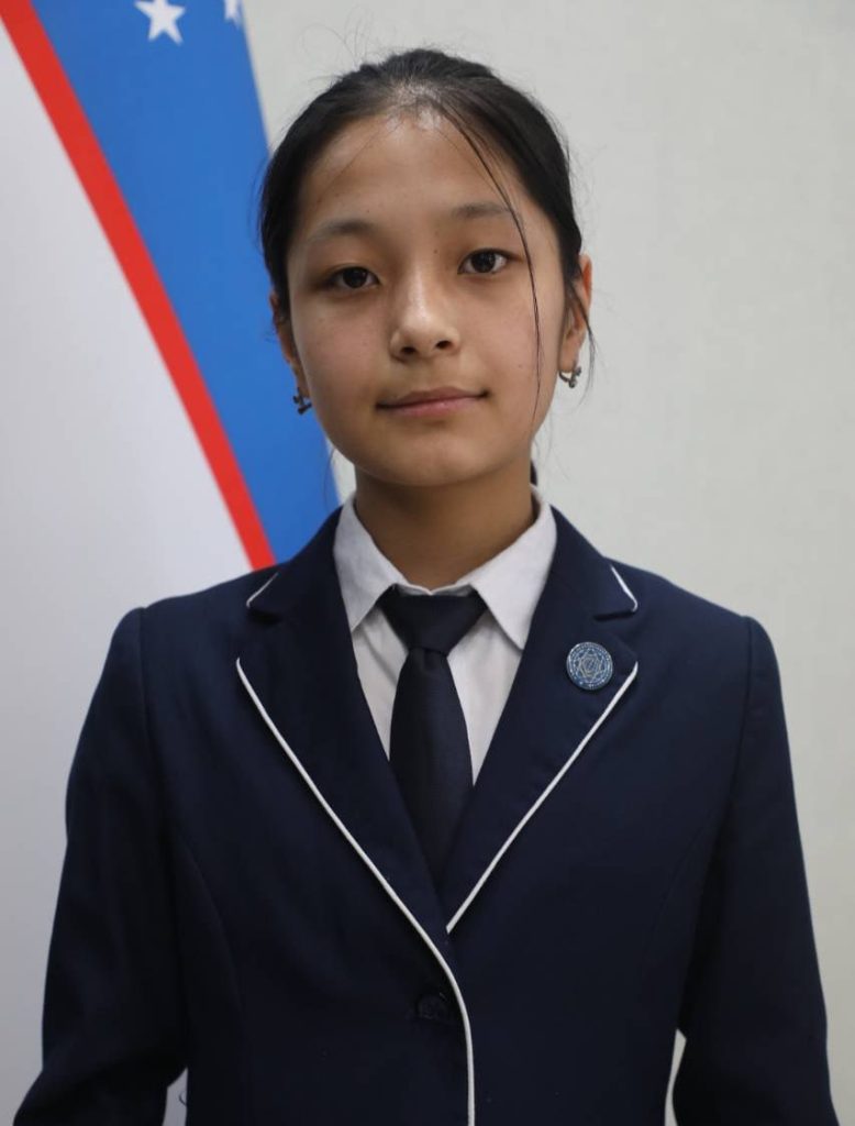 Young Central Asian woman with dark hair up in a bun and in a dark coat and tie and white collared shirt.