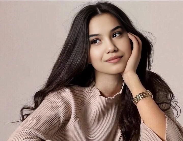 Young Central Asian woman with long dark curly hair, a tan sweater and wristwatch.