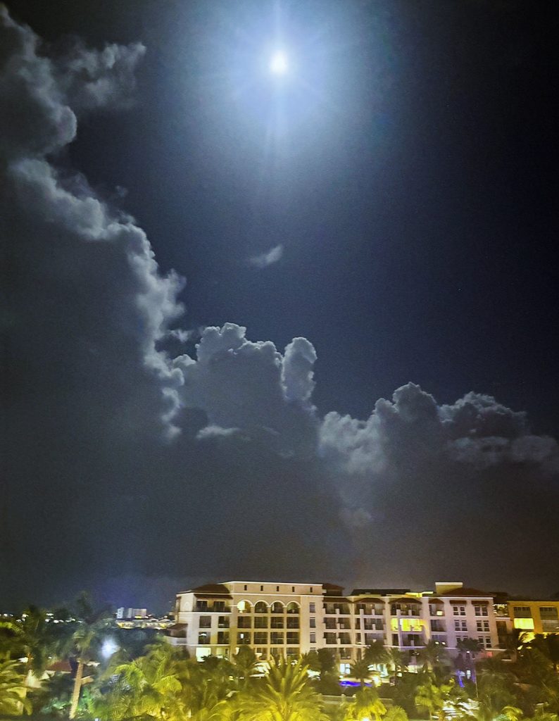 Large multistory resort building with palm trees in front and clouds at night. 