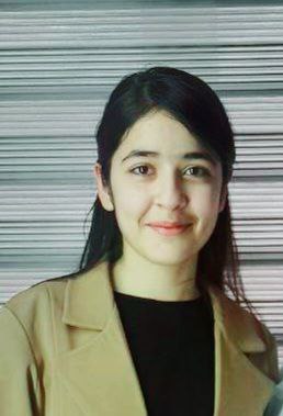 Young Central Asian woman with long straight dark hair and a tan coat over a black blouse.