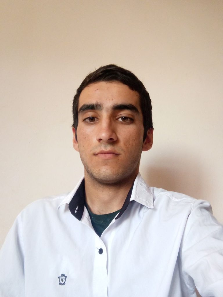 Central Asian man. Young with short dark hair and a white collared sweater over a dark green shirt.