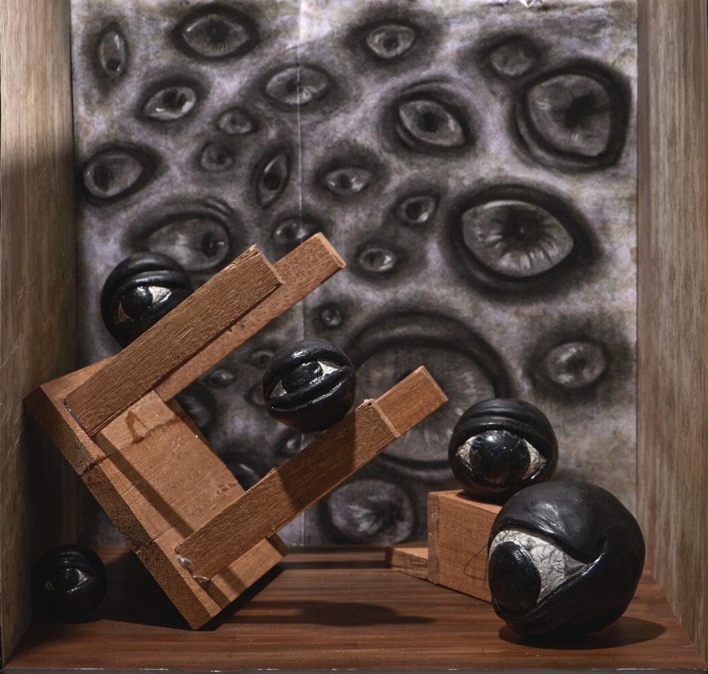 Surreal image of a wooden chair tipped over next to a gray and black canvas full of images of eyes. 