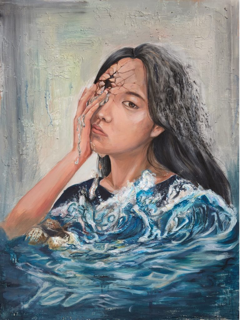 Young woman with long dark hair immersed in blue water puts her hand to her face as she falls apart and crumbles with time. 