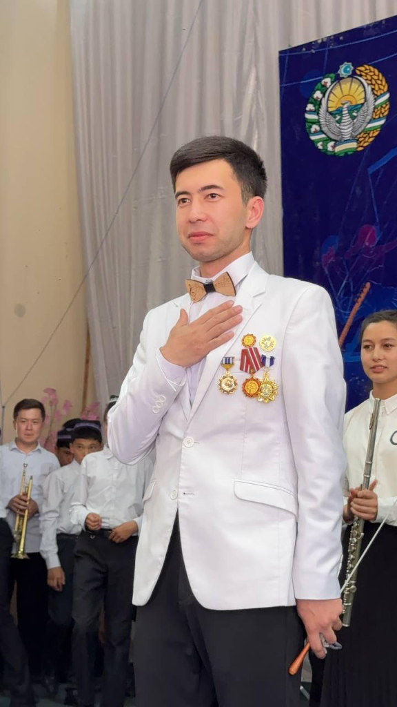 Central Asian man in a white coat and bowtie and medals on his chest and his hand on his heart. 