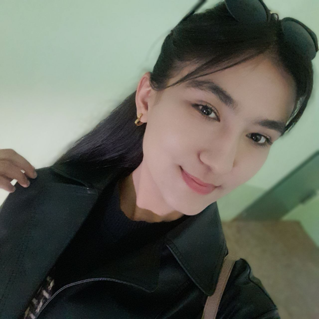 Young Central Asian woman with long dark hair, brown eyes, a black top and coat, and sunglasses on top her head.