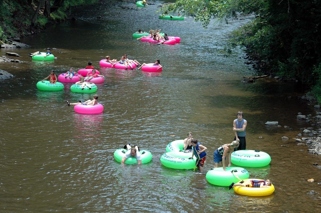 Children in pink and yellow and green inner tubes floating down a river. Rocks and trees on the banks.
