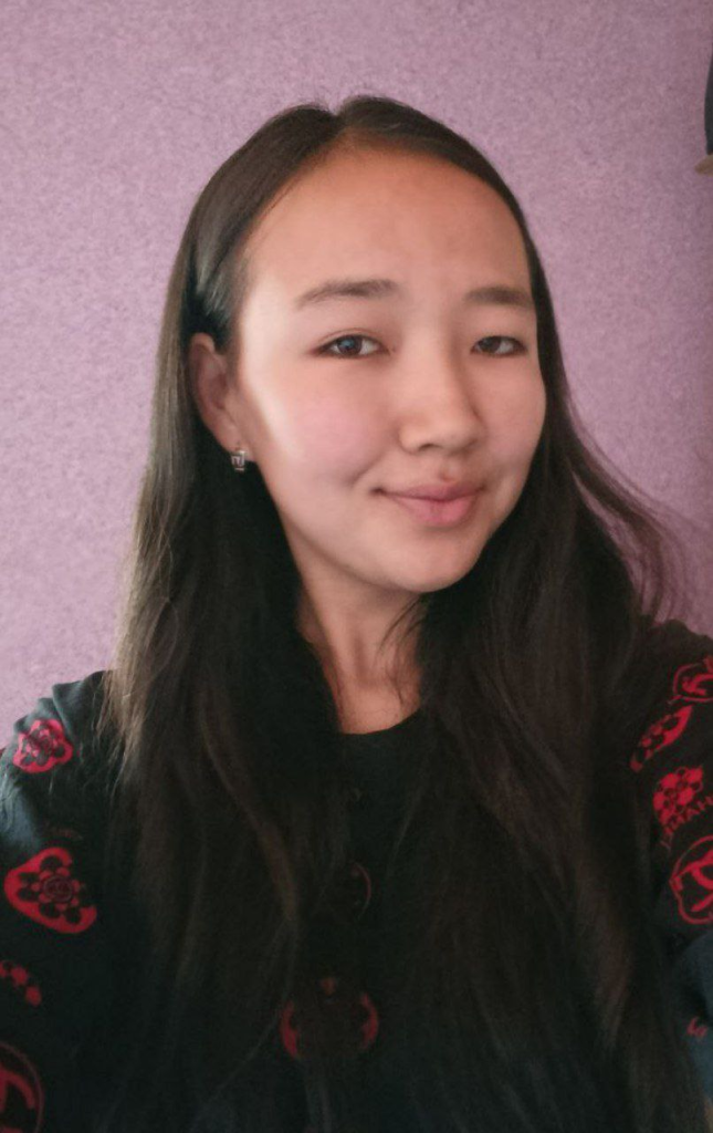 Central Asian woman with long dark hair, small earrings, and a flowered red and black coat over a black top.