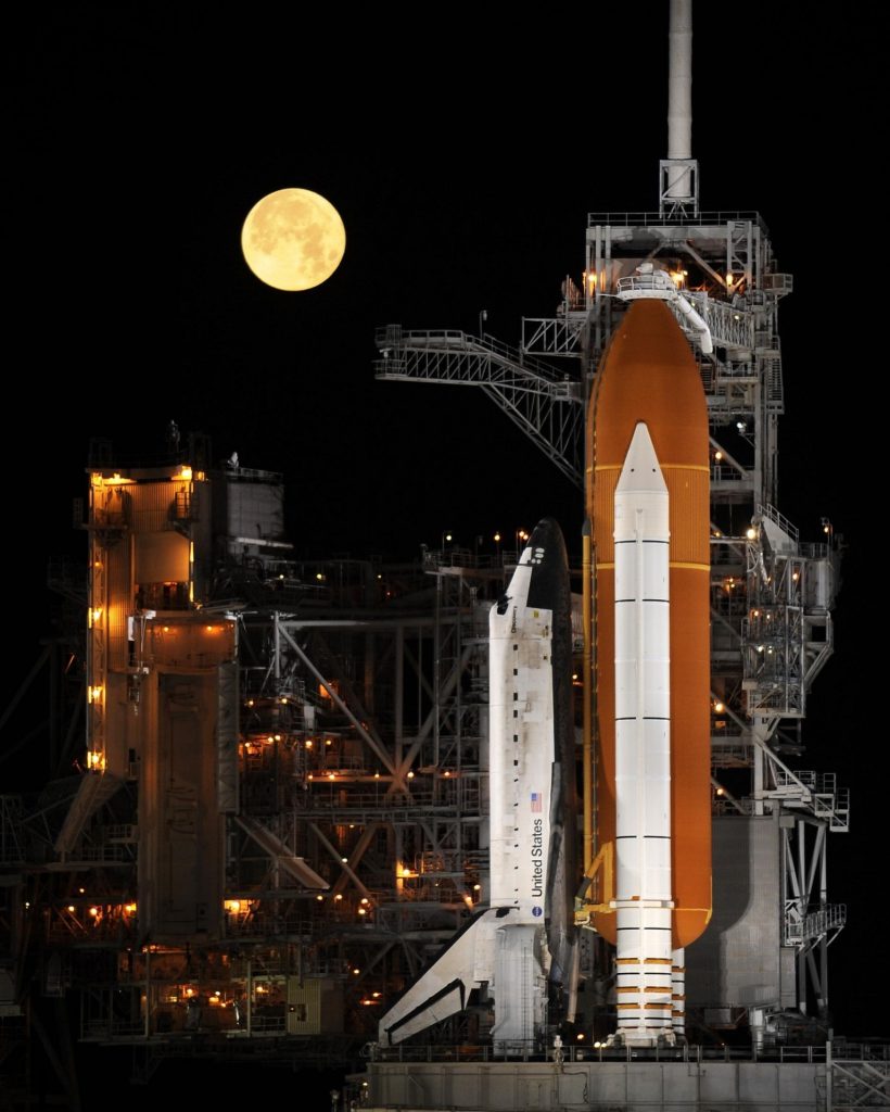 Space shuttle Discovery, with a fuselage and two rockets, under a full moon. 
