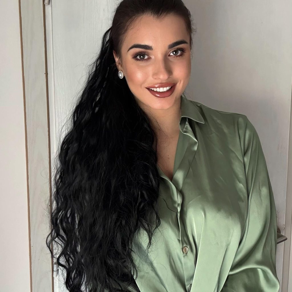 Young Eastern European woman with long dark hair, small earrings, and a light green silk blouse. 