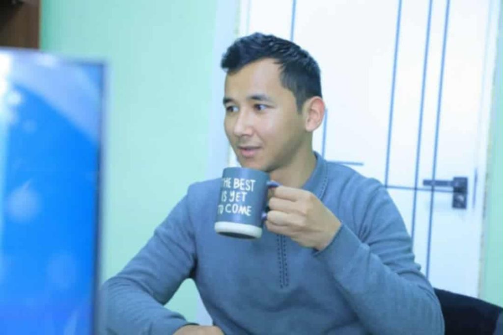 Young middle aged Central Asian man seated in a blue sweater with a coffee cup. 