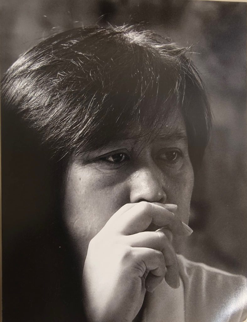 East Asian man with short brown hair and brown eyes resting his head on his hand. Black and white photo. 