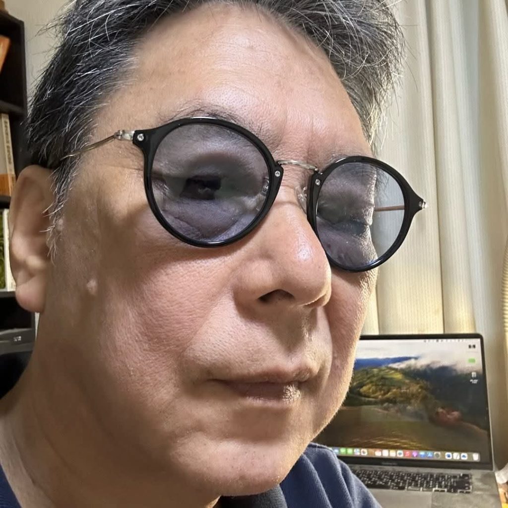 Older East Asian man with short dark hair and reading glasses. 