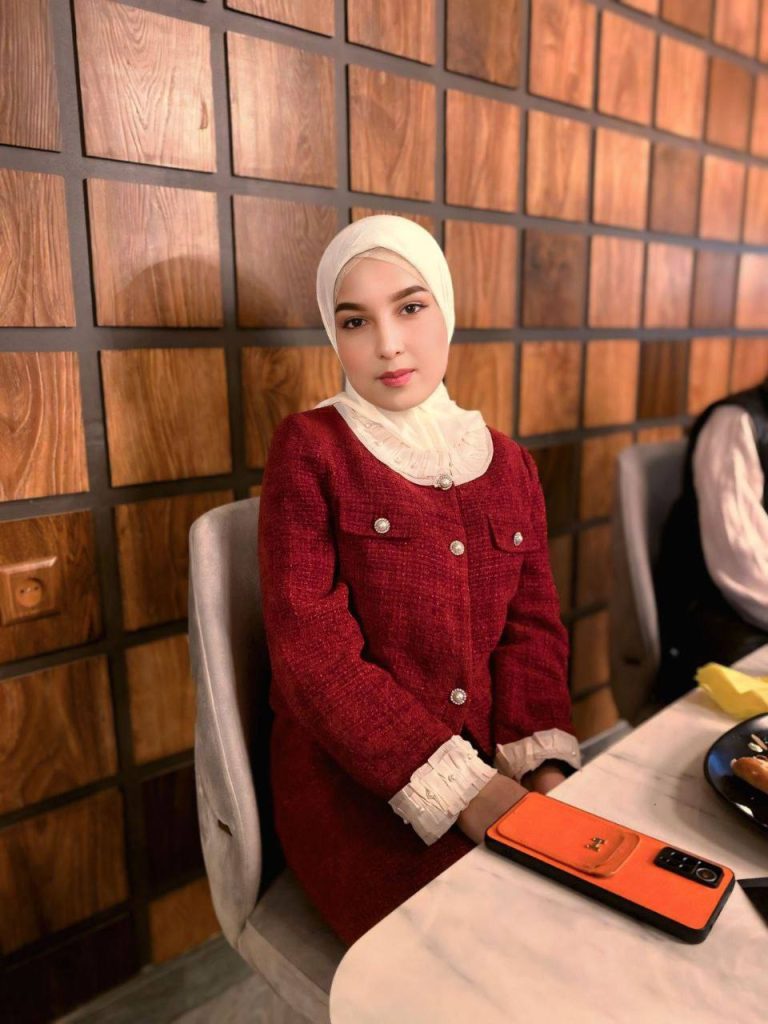 Central Asian woman with a red dress and white headscarf, seated. 