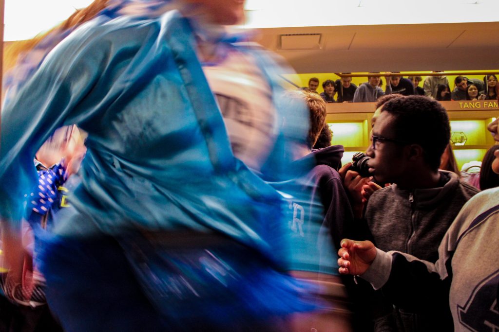 Person with a blue jacket in the foreground dashing through a crowd of other people inside a building. 