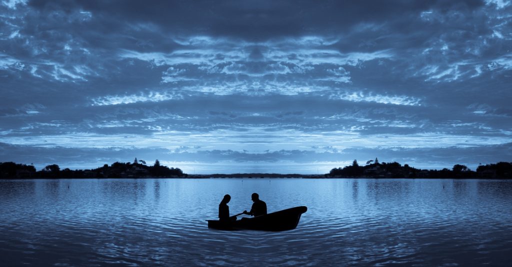 Two silhouetted figures on a paddle boat on a calm lake under a cloudy sky.