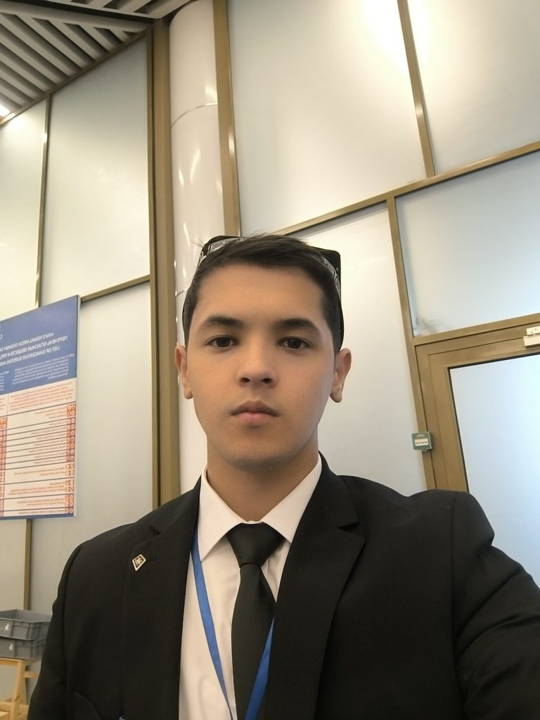 Young Central Asian teen dressed up in a black suit with a white collared shirt and black tie. 