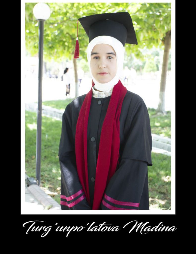 Central Asian woman in a graduation cap and gown with a red tassel, outside by grass on a sunny day.