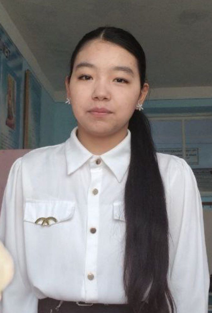 Young Central Asian woman with long dark hair, brown eyes, star shaped earrings, white collared top.