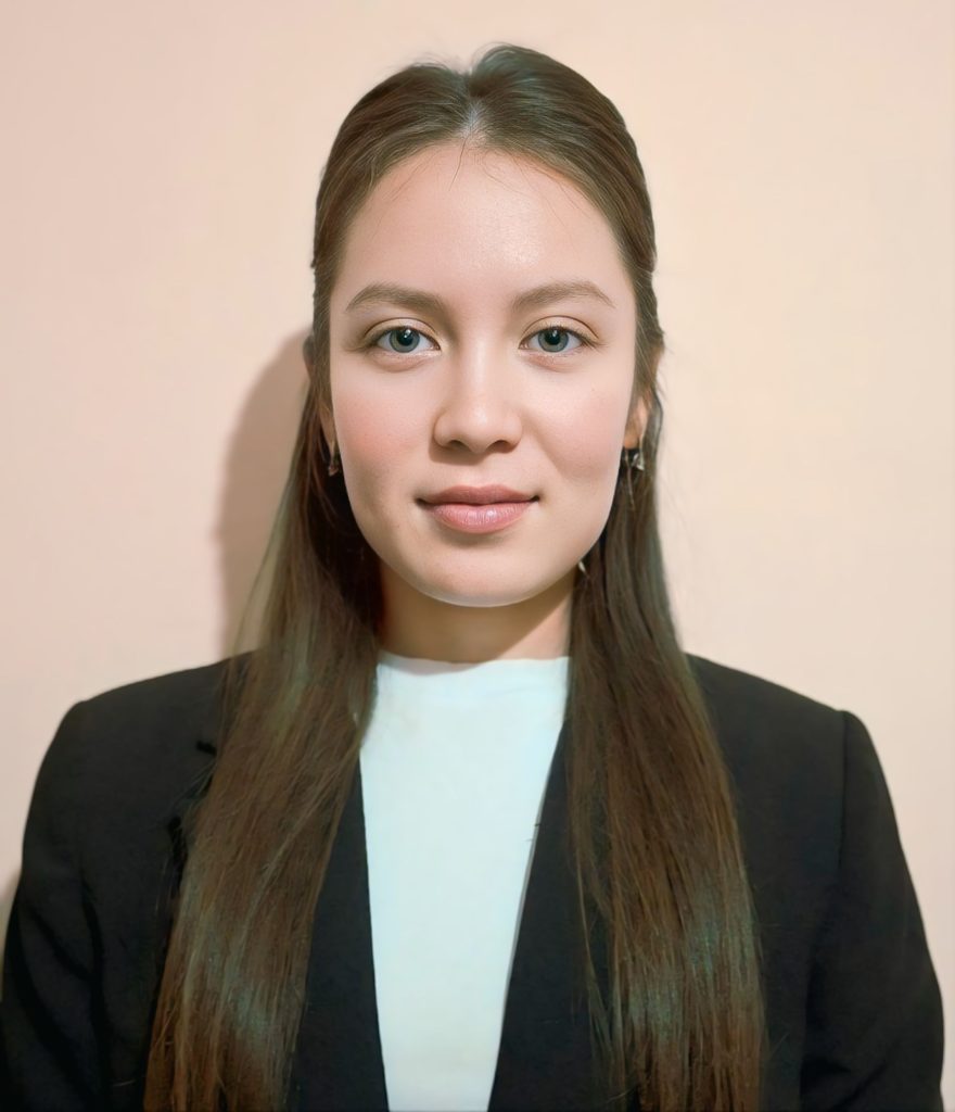 Young Central Asian woman with long dark hair, brown eyes, a black coat and white top.