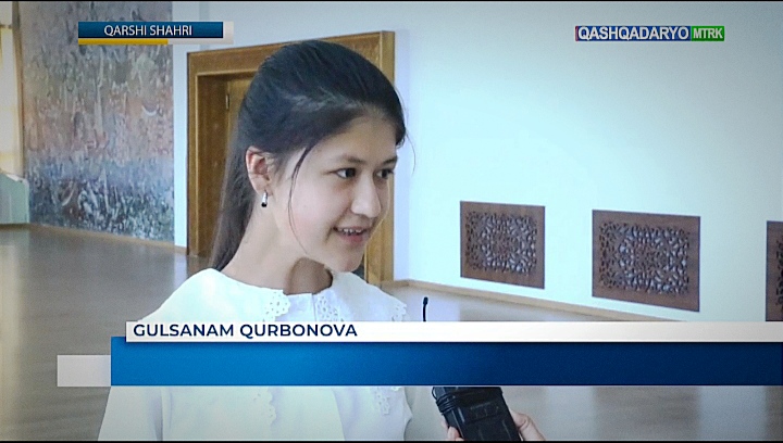 Young Central Asian woman with straight dark hair and brown eyes and a white blouse, speaking in a museum.