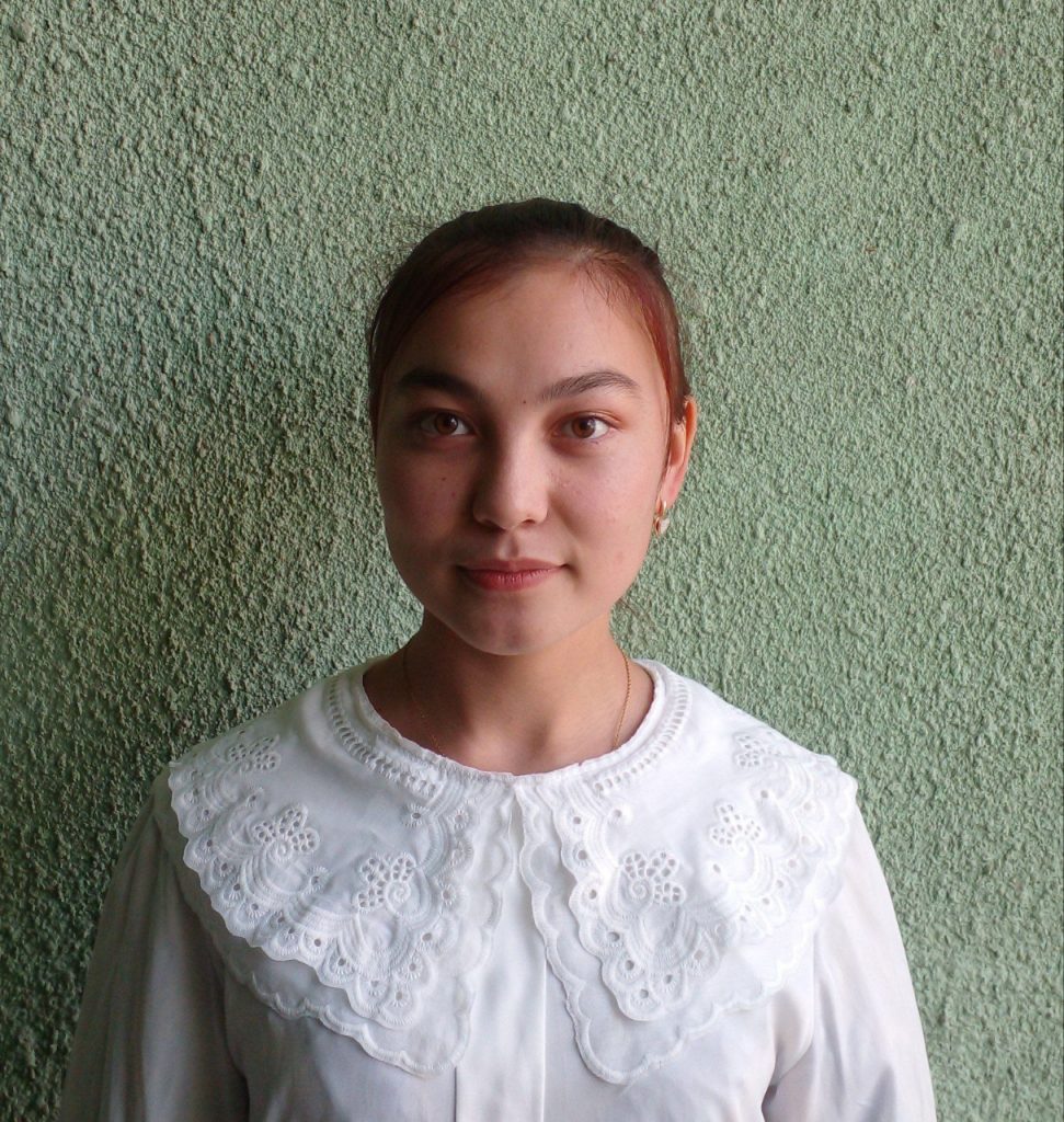 Young Central Asian woman with her hair in a bun behind her heard and a white ruffled blouse.