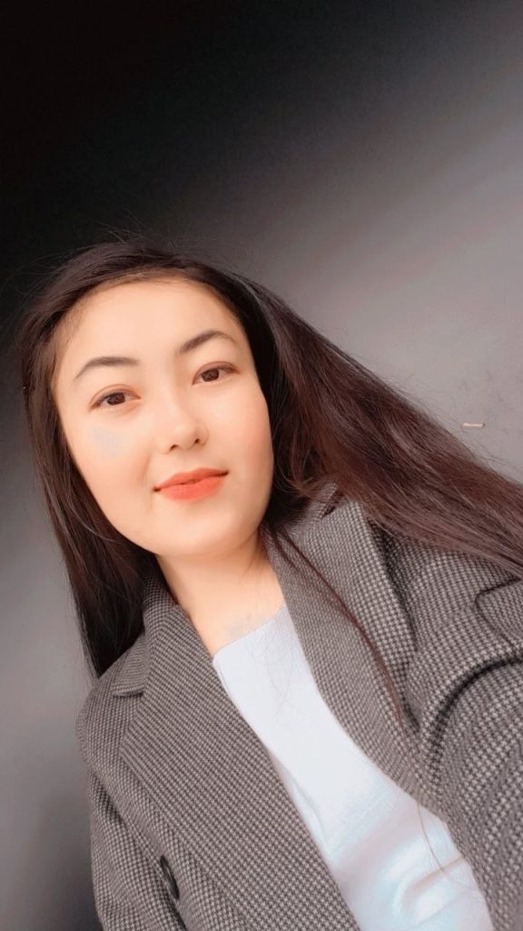 Central Asian woman with long dark hair and a black and white coat and a top.