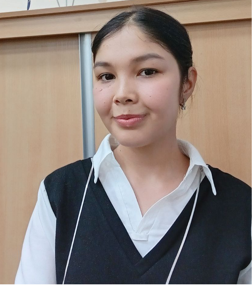 Young Central Asian woman with straight dark hair in a bun behind her head, small earrings, and a white collared shirt and black coat.